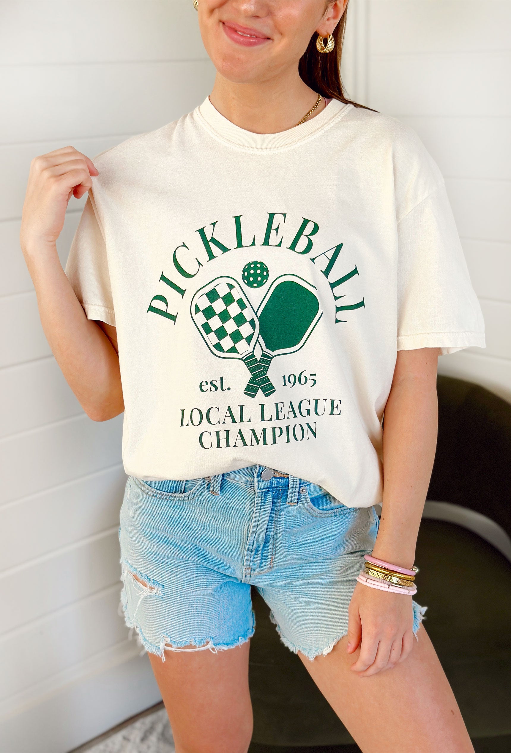 Friday + Saturday: Pickleball Local League T-Shirt, cream short sleeve t-shirt with "Pickleball est. 1965 local league champion" in green with pickleball paddle graphics in green 