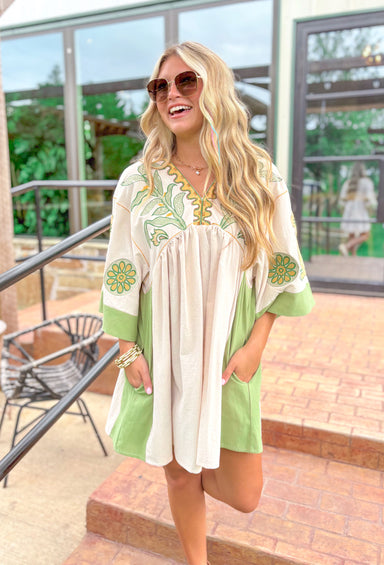 All For You Dress, beige base with muted green detailing down the sides and around the bottom of the sleeves, embroidered leaf and flower details around the chest and on the sleeves in muted green, kelly green and yellow 