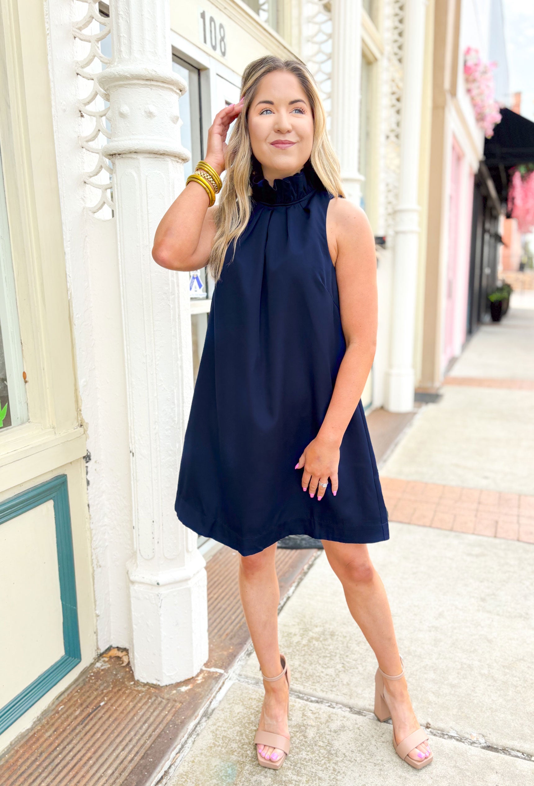 Capri Calling Dress in Navy, Navy sleeveless high neck dress, ruffling around the neck, bow detail on the back of the neck that drapes down the back