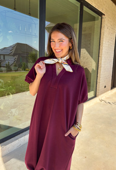 Effortless and versatile, this burgundy midi dress is an easy favorite for fall. Designed with a band collar v-neckline and elasticated short sleeves, it offers both structure and comfort. Side pockets keep it practical, while the soft, stretchy fabric blend makes it perfect for all-day wear. You'll find yourself reaching for this dress all season long!