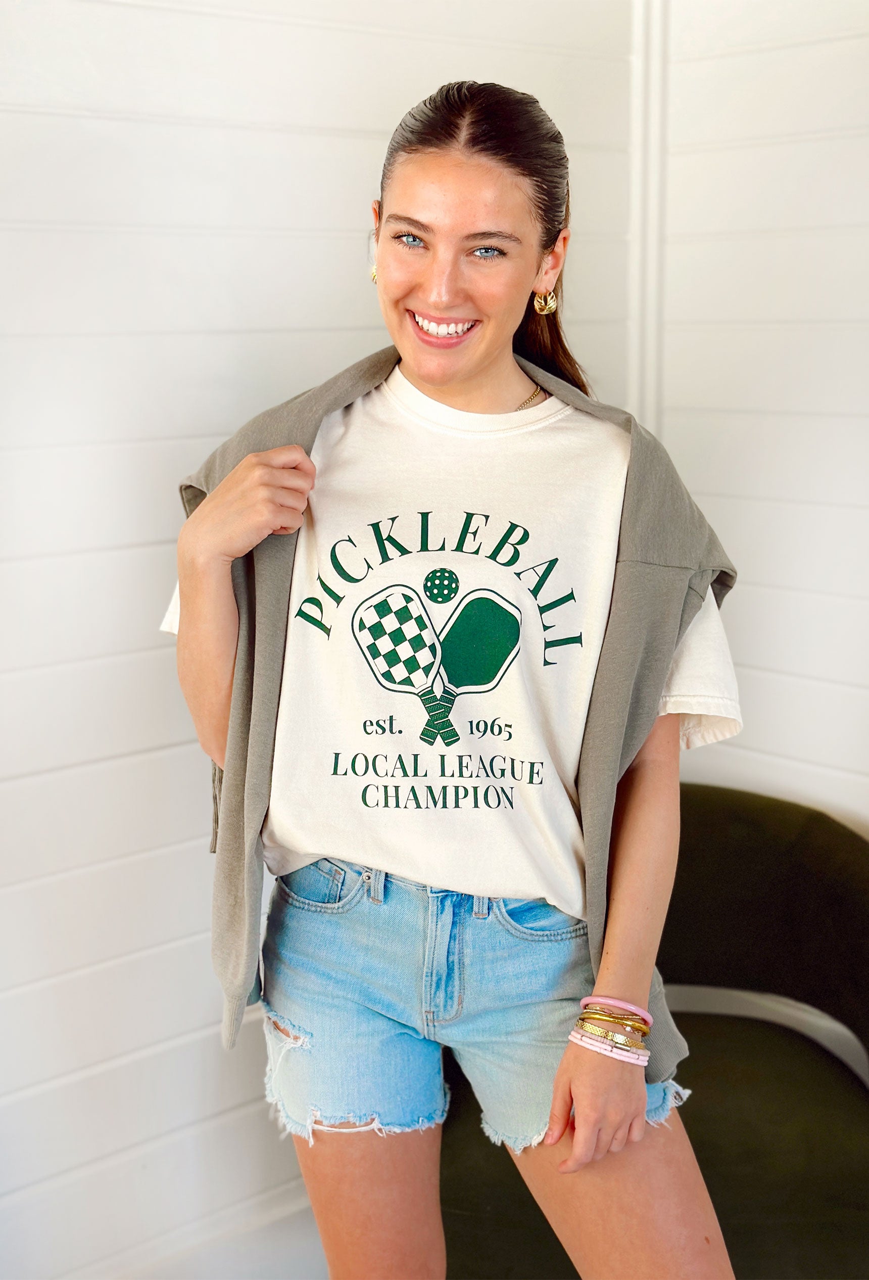 Friday + Saturday: Pickleball Local League T-Shirt, cream short sleeve t-shirt with "Pickleball est. 1965 local league champion" in green with pickleball paddle graphics in green 