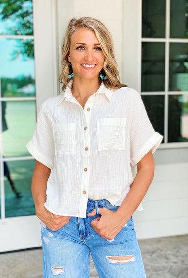 Southern Shores Gauze Button Up Top. Lightweight top with white gauze fabric and wooden buttons. Has two front pockets and a rolled sleeve.