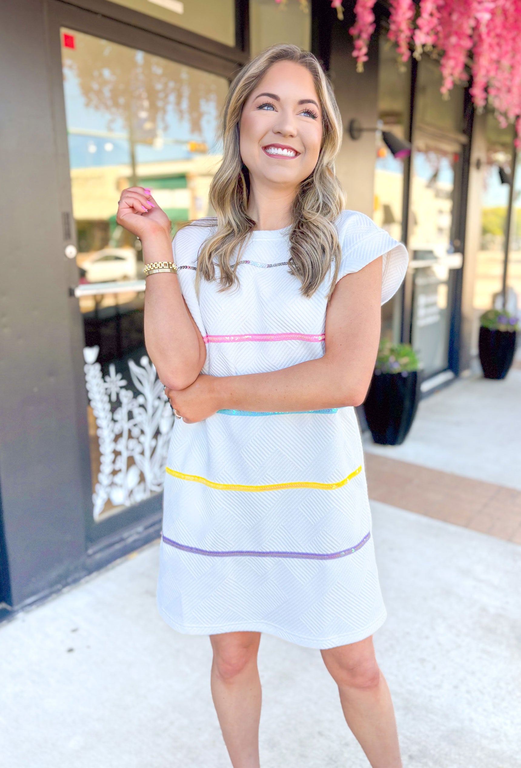 All The Attention Dress in White, short sleeve white textured dress with pockets, silver, baby pink, electric light blue, yellow, & purple horizontal sequin stripes on the dress