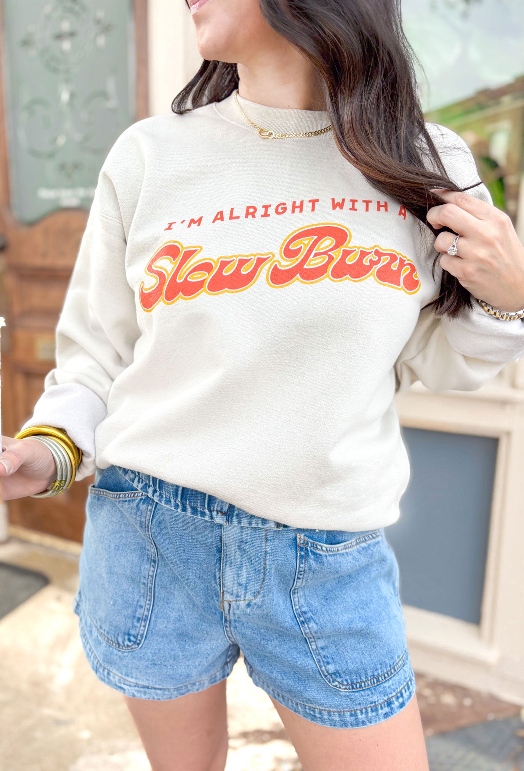 Charlie Southern: Slow Burn Sweatshirt, tan crewneck with front graphic in red and yellow saying "i'm alright with a slow burn" on the back is different match boxes in the colors red, pink, yellow, orange, and white