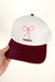 Charlie Southern: Texas Bow Trucker Hat, trucker hat with white base and maroon bill, pink embroidered bow in the center with maroon "Texas" underneath it 