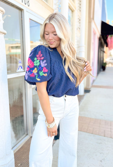Couldn't Be Better Blouse, short puff sleeve blouse in navy with v-neck, embroidered floral print on the sleeves in the colors green, fuchsia, yellow, and lilac
