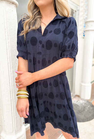 Hope You Know Dress in Navy, gauze dull navy short sleeve v-neck dress with a collar, textured polkadots all over the dress, tiering, raw bottom hem, cinching at the bottom of the sleeves