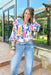 Taking The Leap Blouse, quarter sleeve blouse with cream floral print, background and other patterns are pink, blue and yellow. Round neck line and ruffling on the end of the sleeve