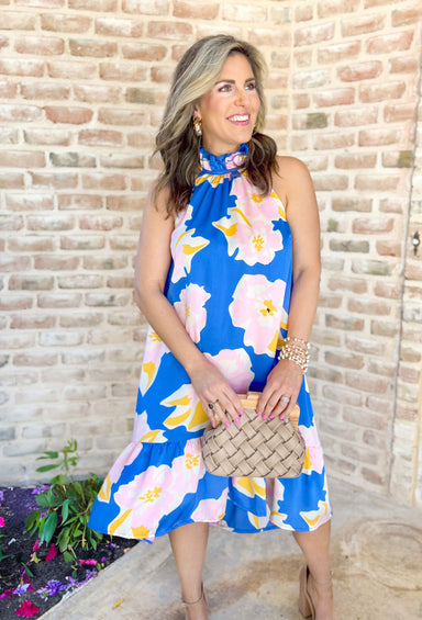 When You're Mine Dress, cobalt sleeveless high neck dress with ruffling on the neck. Floral pattern across the dress in light pink, white, and yellow with tier detail on the bottom of the dress