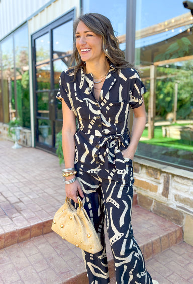 You're The Reason Jumpsuit, black short sleeve jumpsuit with white line designs across the whole piece. button down to the waist and tie detail around the waist