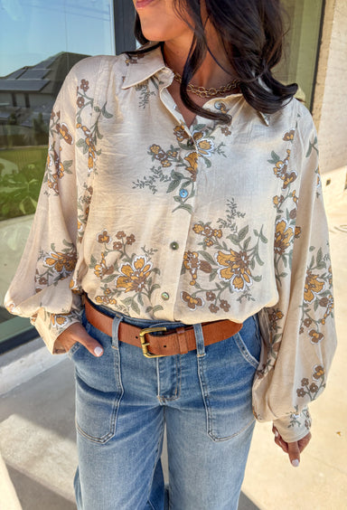 Soft and romantic, this ecru button-down top brings autumn tones to life with its neutral floral print. The flowy silhouette and lightweight fabric make it comfortable and easy to wear, while balloon sleeves add volume and charm. Perfect for layering or styling on its own, this top transitions seamlessly from weekday polish to weekend casual.