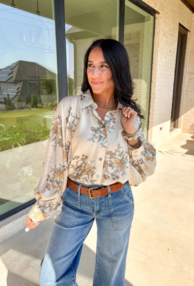 Soft and romantic, this ecru button-down top brings autumn tones to life with its neutral floral print. The flowy silhouette and lightweight fabric make it comfortable and easy to wear, while balloon sleeves add volume and charm. Perfect for layering or styling on its own, this top transitions seamlessly from weekday polish to weekend casual.