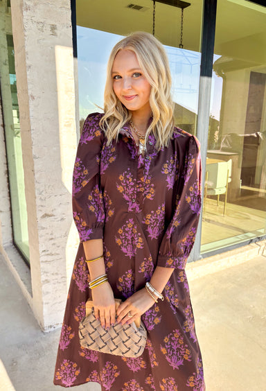 Earthy tones meet feminine charm in this beautiful botanical print midi dress by Entro. Designed with ¾ sleeves and a soft ruffle trim along the collar and front placket, it’s full of subtle details that make it feel special. The button-front design and side pockets bring functionality, while the brown base with purple and dark yellow florals gives it that perfect fall color palette. Fully lined and made from breathable cotton, it’s comfortable enough for all-day wear while keeping your look effortlessly po