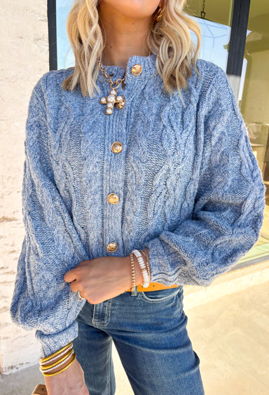 Cozy meets classic in this chambray blue cable knit cardigan. The textured knit adds timeless charm, while gold accent buttons bring a touch of polish that’s perfect for the season. Designed with long sleeves and a slightly relaxed fit, it’s the kind of layer you can throw on over a dress for a coffee date or pair with jeans for everyday wear. Soft, warm, and endlessly versatile, this cardigan is ready to be your go-to as the weather cools.