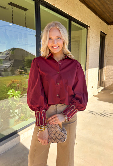 This burgundy button-down top by Jodifl brings unique embroidered detailing to a classic silhouette. The collar features intricate embroidery in olive, rust, and tan, while the sleeves showcase a coordinating abstract embroidered design in the same earthy tones—adding contrast and personality to the look. Crafted from 100% cotton, it’s breathable, lightweight, and perfect for styling through the season.