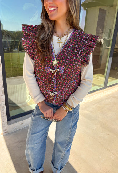 This charming quilted vest is giving all the cozy fall vibes with a pop of cheerful color. The brown base is covered in a dainty floral print in soft shades of pink, orange, and green—perfect for layering over your favorite long sleeve tops. Ruffle sleeves and oversized button closures add just the right amount of whimsy!