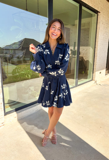 Delicate details and a flowy fit make this navy dress a true fall favorite. Embroidered with an off-white leaf print throughout, it strikes the perfect balance of playful and polished. The collared neckline and button-down front add structure, while the self-tie waist flatters your shape. Finished with buttoned cuffs and a flowy skirt, this fully lined dress is both comfortable and chic—ready for anything from weekday wear to seasonal celebrations.