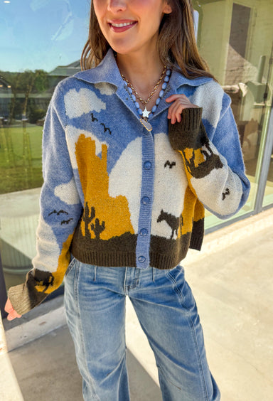Cozy meets western charm in this light blue button-down cardigan. The collared neckline gives it structure, while the playful scene—complete with clouds, cactus, birds, and horses—adds a whimsical fall touch. Crafted in a soft knit blend with plenty of stretch, it’s a comfortable piece that’s as unique as it is versatile. Easy to style open or closed, this cardigan is the perfect way to add personality to your autumn wardrobe.