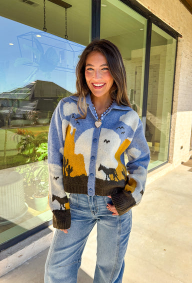 Cozy meets western charm in this light blue button-down cardigan. The collared neckline gives it structure, while the playful scene—complete with clouds, cactus, birds, and horses—adds a whimsical fall touch. Crafted in a soft knit blend with plenty of stretch, it’s a comfortable piece that’s as unique as it is versatile. Easy to style open or closed, this cardigan is the perfect way to add personality to your autumn wardrobe.