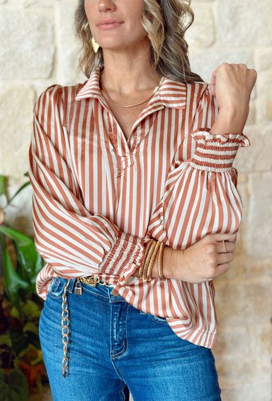 As You Are Striped Blouse, satin long sleeve striped blouse in rust and cream. Top has a collar and cinched wrists with ruffling on the hem