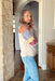 Aspen Plans Sweater, tan turtle neck sweater with orange, denim, periwinkle, lilac, burgundy, and pale yellow stripes on the sleeves and over the chest. Cream and lilac abstract shapes on top of the stripes 