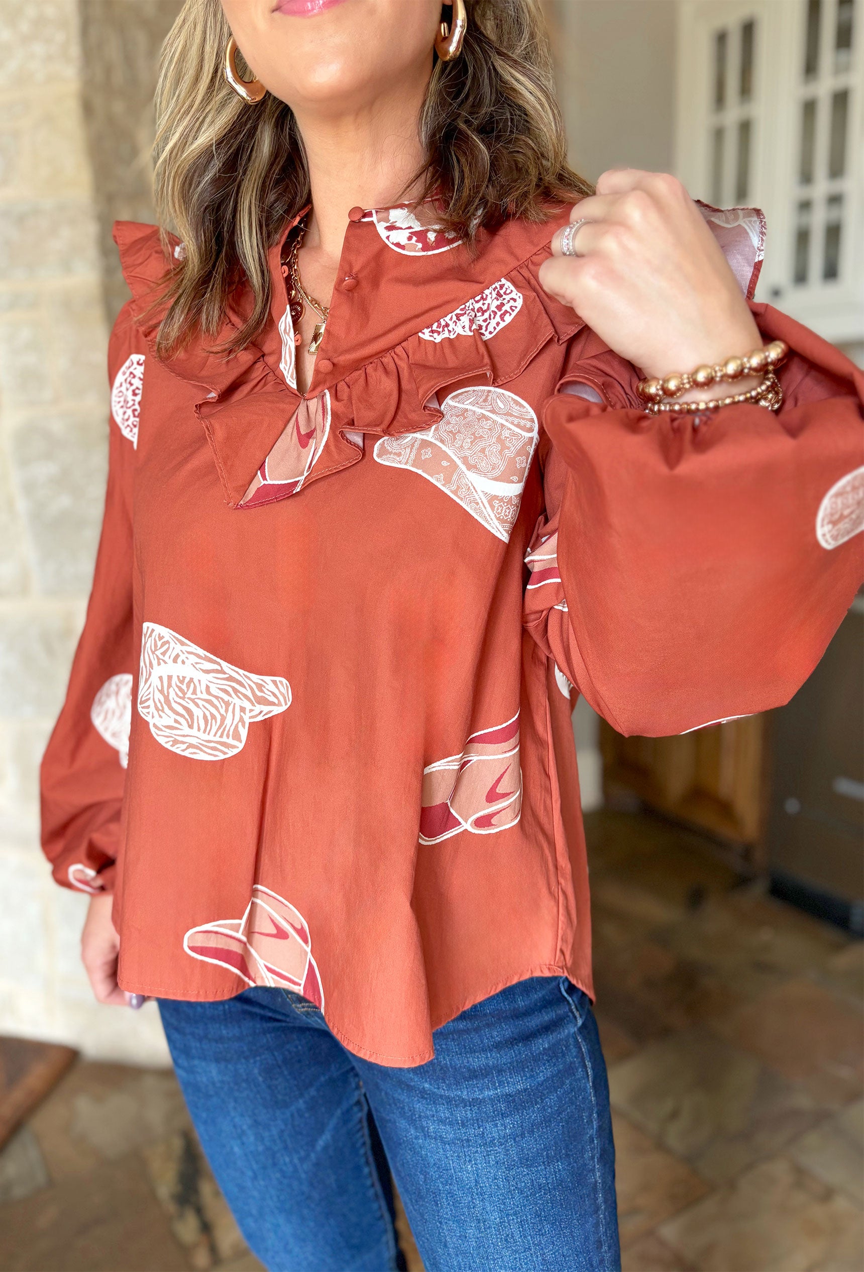 Cowboy Take Me Away Blouse, burnt orange blouse with ruffling across the chest and graphic cowboy hats all over the blouse