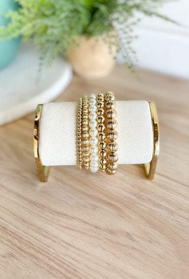 My Little Secret Bracelet Set, stack of 5 bracelets varying in size, 4 gold beaded one pearl beaded, two gold beaded bracelets are textured two are smooth
