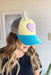 Turquoise, yellow, and gray trucker hat decorated with a purple heart patch outlined in gold glitter.