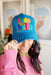 Judith March Taco Belle Hat,  Blue and tan trucker hat decorated with "Taco Belle" multicolor patch outlined in gold glitter, and subtle distressing with scratch detail